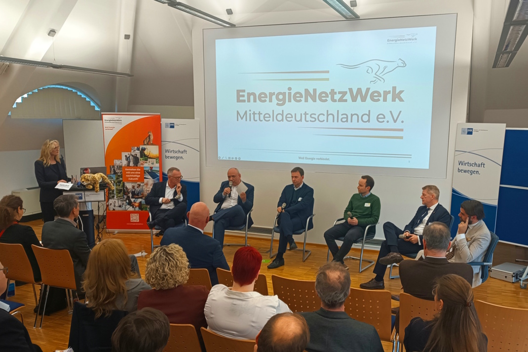 Mehrere Menschen bei Podiumsdiskussion auf einer Bühne vor Zuschauern in einem geschlossenen Raum.