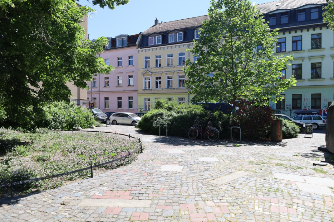 Der Westentaschenpark in Lindenau, Sonnenschein und grüne Bäume, Hausfassaden im Hintergrund.