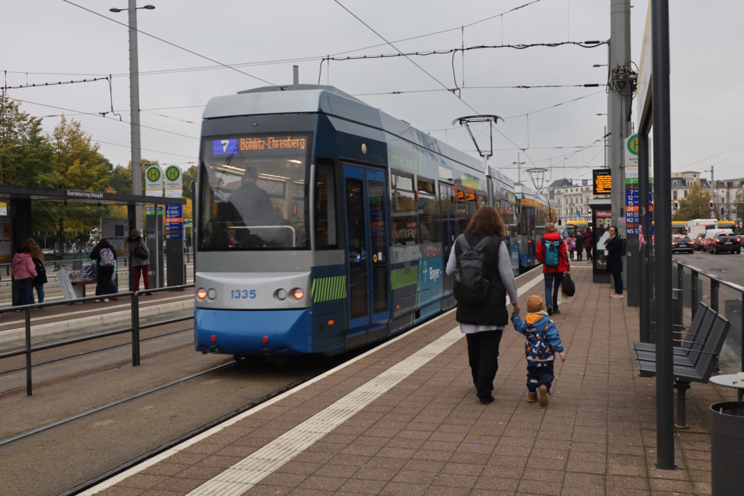 Tram-Haltestelle, stehende Straßenbahn und Passanten.
