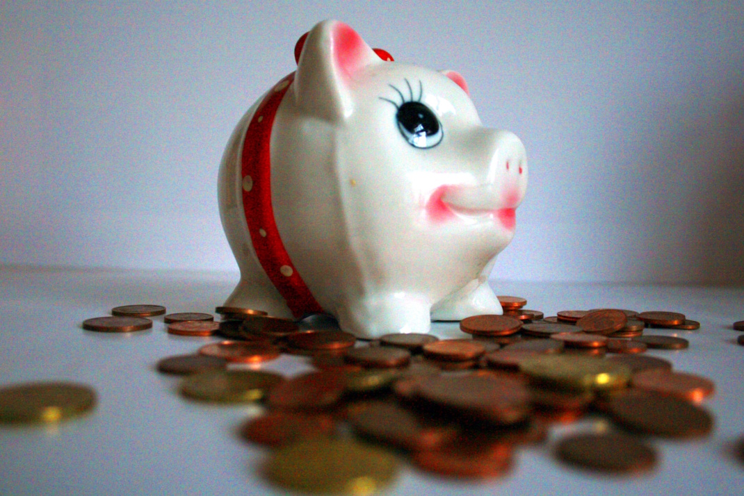 Aufgehäufte Münzen neben einem Sparschwein, Nahaufnahme.