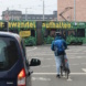 PKW, rechts daneben ein wartender Radler und eine Straßenbahn im Hintergrund.