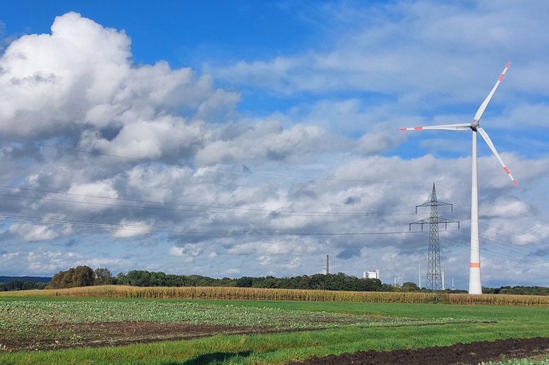 Windrad in der Landschaft, blauer Himmel und Wolken.