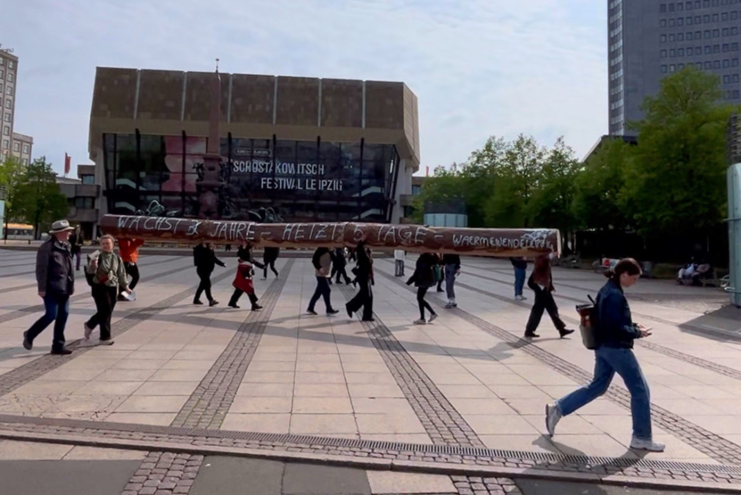 Symbolischer Baumstamm wird über einen öffentlichen Platz getragen.