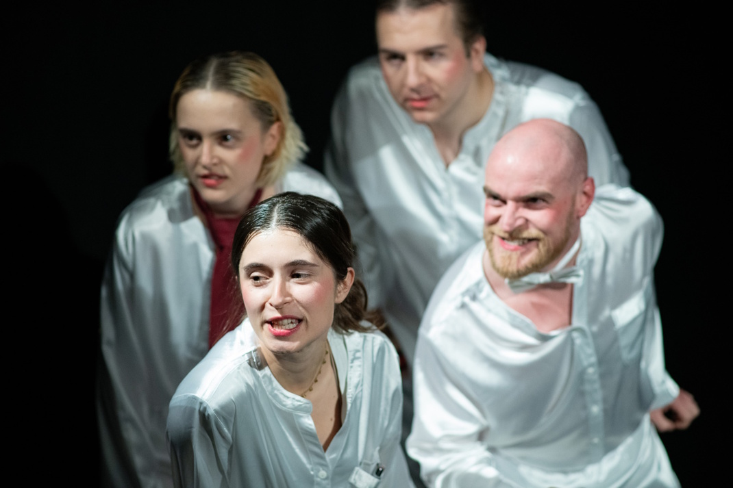 Mehrere Schauspieler, in hellen Gewändern, Theaterszene.