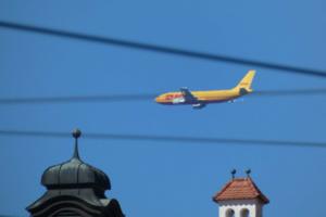 DHL-Flugzeug am Himmel. Dazu Oberleitungen und Türmchen.