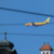 DHL-Flugzeug am Himmel. Dazu Oberleitungen und Türmchen.