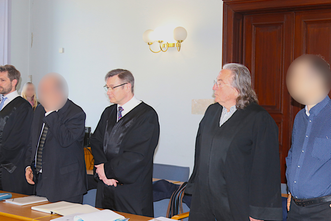 Zwei unkenntlich gemachte Personen stehen mit ihren Anwälten an der Anklagebank des Landgerichts.