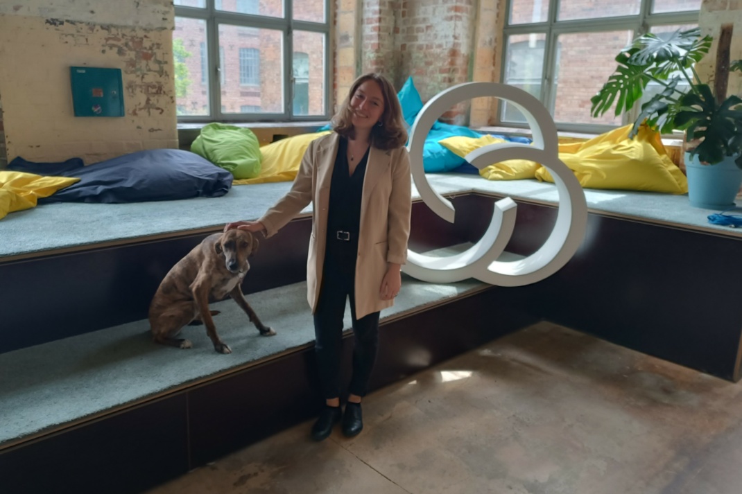 Junge Frau mit Hund vor Treppe mit Sitzkissen und Fensterfront, rechts Logo SpinLab