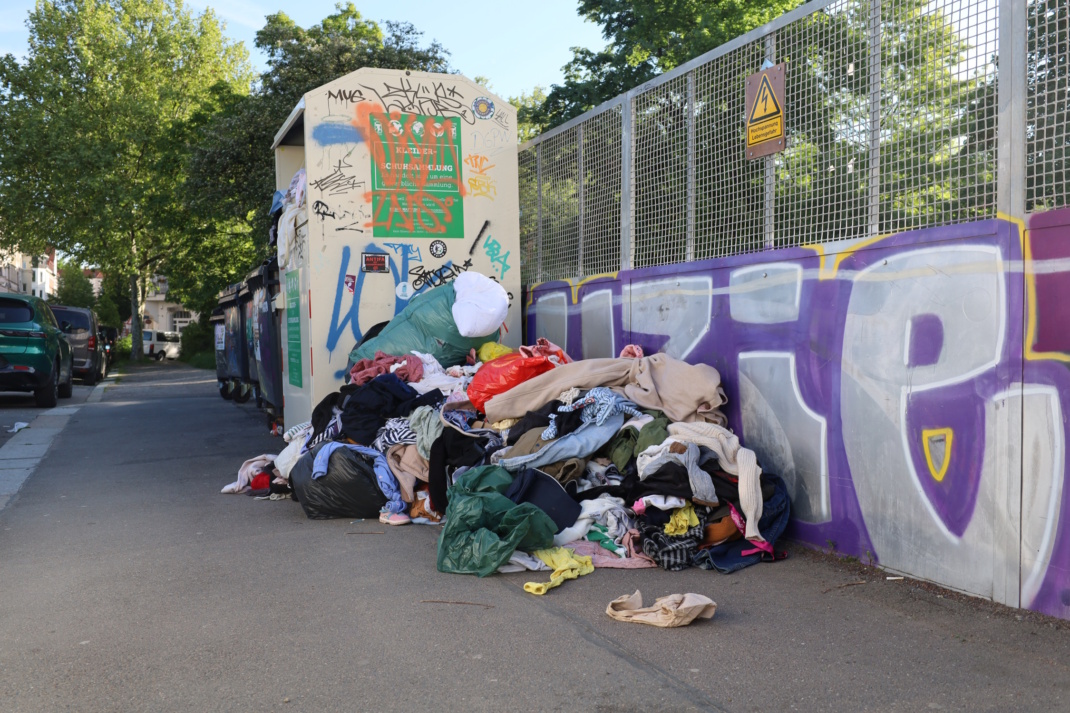 Alttextilien häufen sich neben dem vollen Kleidercontainer.