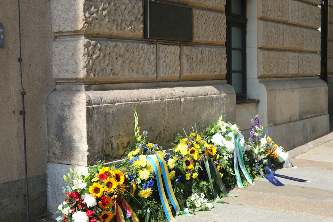 Kränze liegen an Hauswand mit Plakette.
