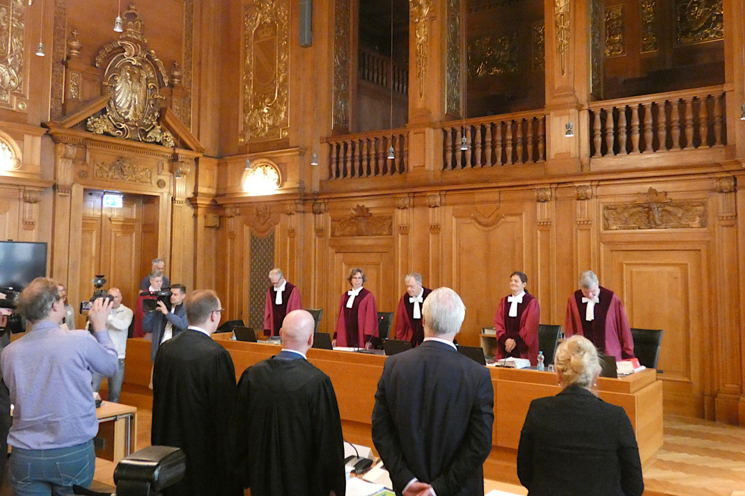 Mehrere Personen vor einer Richterbank, Richter in roten Roben.