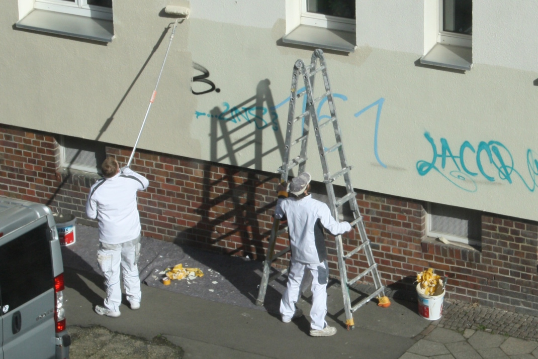 Maler, die an einer Hauswand Graffiti beseitigen.