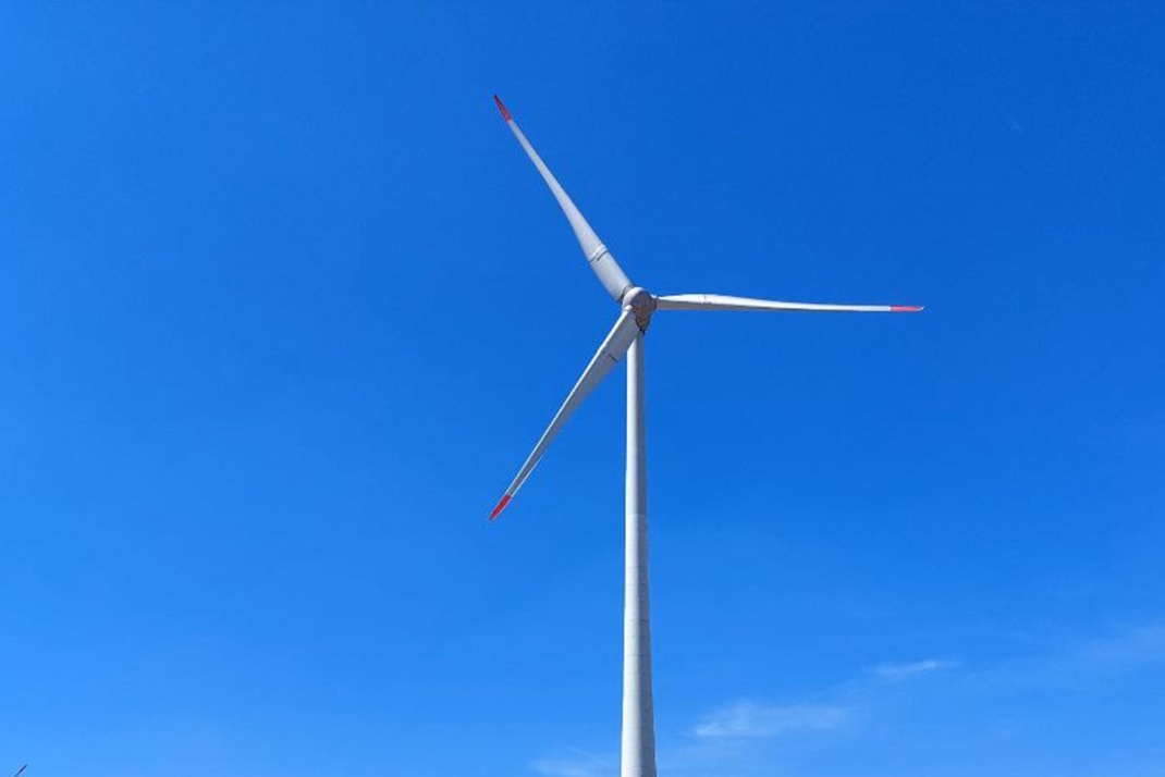 Windrad vor sommerlich blauem Himmel.