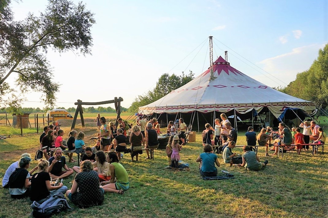 Menschen sammeln sich auf der Wiese vor einem Zirkuszelt.