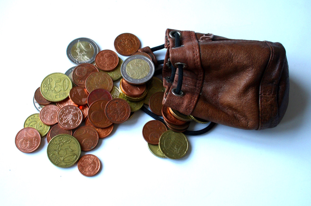 Euro- und Centstücke, die aus einem Beutel heraus aufgehäuft liegen.