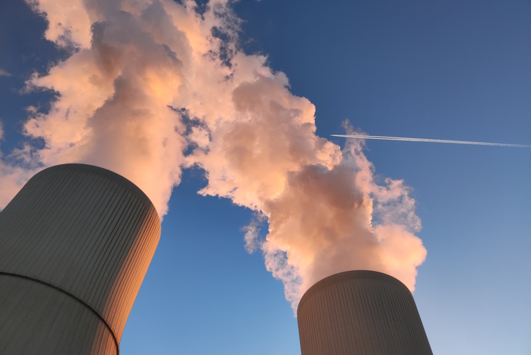 Kühltürme des Kohlekraftwerks Lippendorf, rauchende Schlote vor blauem Himmel.