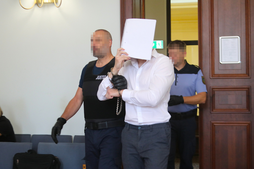 Angeklagter wird in Handschellen hereingeführt.