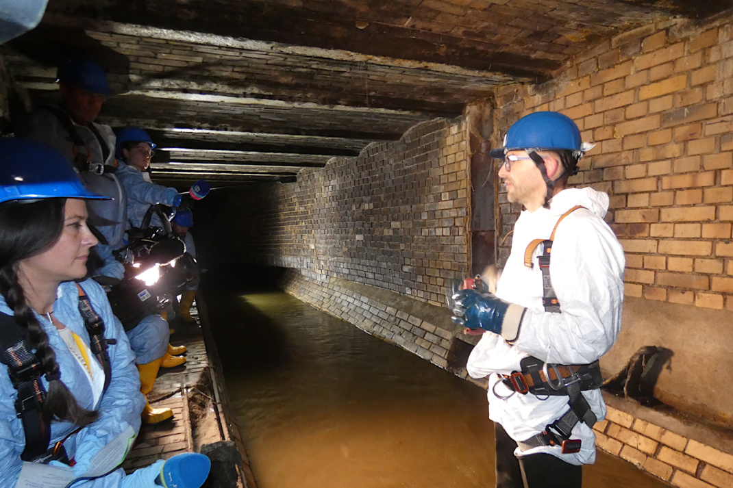 Mann im weißen Schutzanzug steht in Kanalisation.
