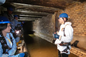 Mann im weißen Schutzanzug steht in Kanalisation.
