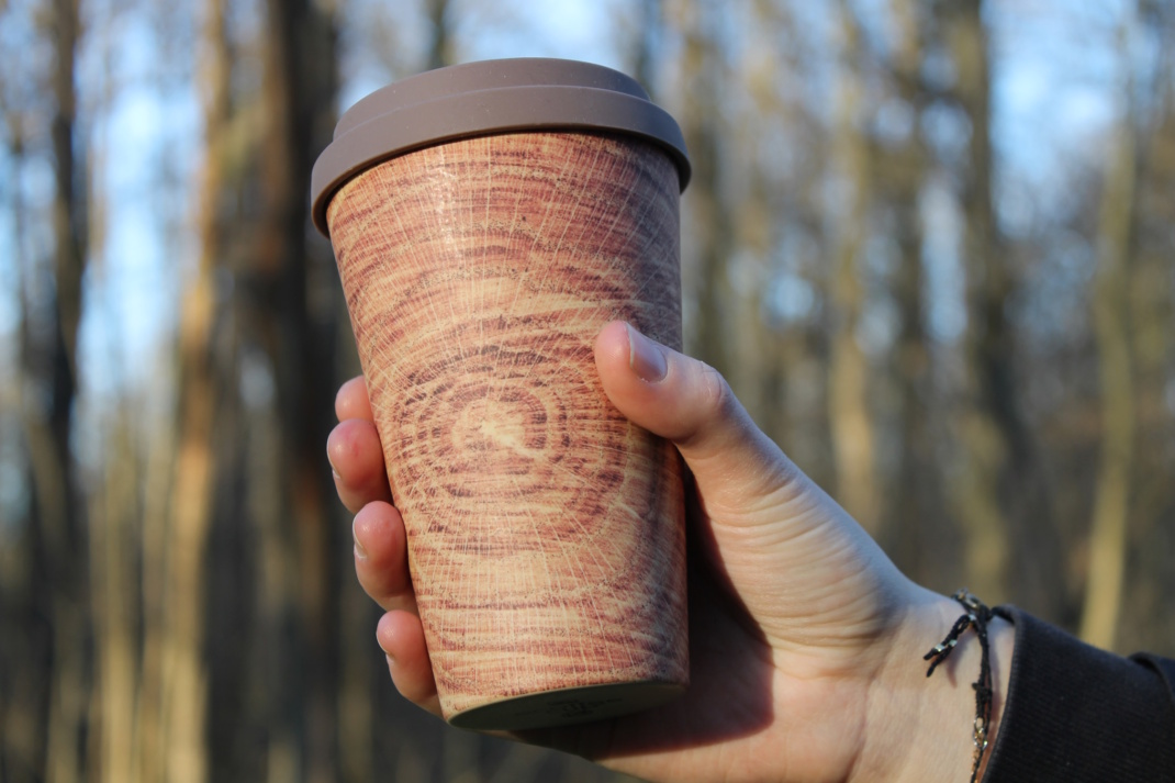 To-Go-Becher mit Holztarnung, in einer Hand gehalten.