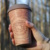 To-Go-Becher mit Holztarnung, in einer Hand gehalten.