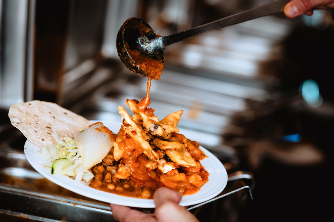 Hand hält vollen Buffet-Teller, über den eine Kelle schwingt.