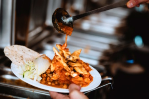 Hand hält vollen Buffet-Teller, über den eine Kelle schwingt.