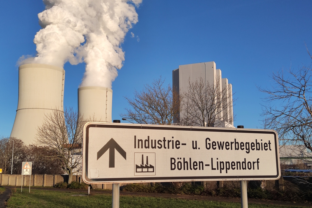 Kraftwerk mit Hinweisschild und rauchenden Schloten.