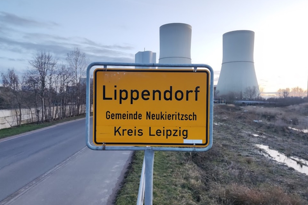 Ortsschild zu Lippendorf, Türme des Kraftwerks im Hintergrund.