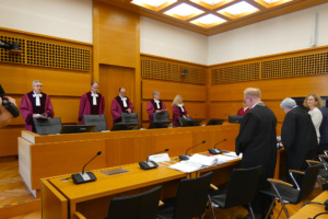 Richter in roten Roben stehen im Gerichtssaal hinter der Bank und schauen entgegen der Kamerarichtung.