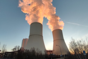 Kohlekraftwerk, rauchende Schlote, in denen sich Sonnenlicht spiegelt.