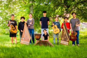 Gruppe junger Menschen mit Musikinstrumenten steht auf einer Wiese im Park.