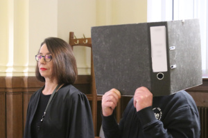 Angeklagter steht hinter Ordner im Gericht neben seiner Anwältin.