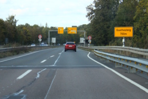 Befahrene Straße aus Autofahrer-Perspektive, Auto in einiger Entfernung.