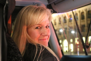 Blondhaarige Frau hat den Kopf nach rechts gedreht und schaut zur Kamera.