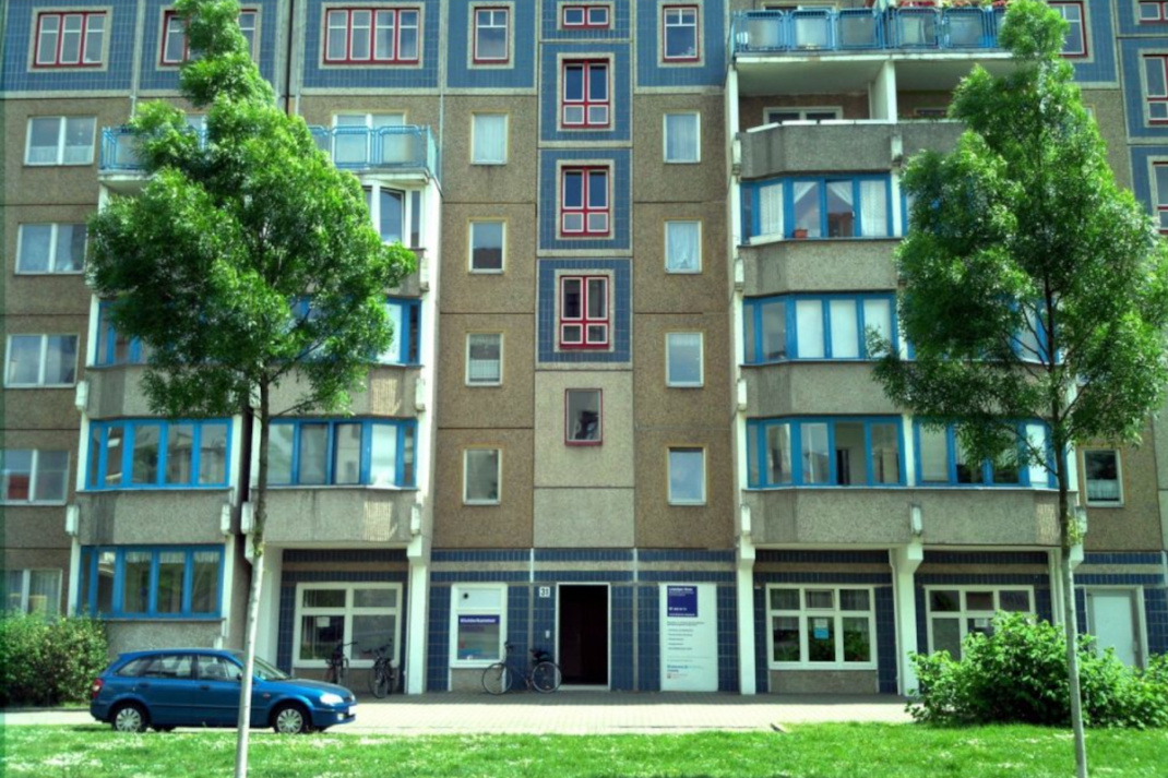 Hausfassade mit Bäumen und Wiese.