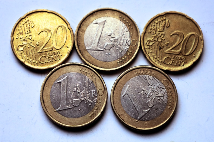 Aufgereihte Euromünzen liegen in zwei Reihen auf heller Fläche.