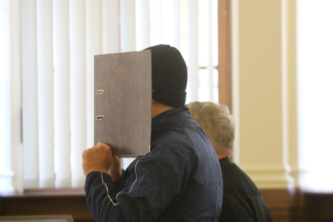 Mann mit Ordner vor dem Gesicht im Gerichtssaal