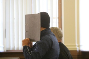 Mann mit Ordner vor dem Gesicht im Gerichtssaal