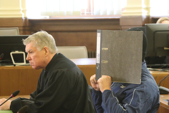 Angeklagter mit Sichtschutz sitzt neben Anwalt.