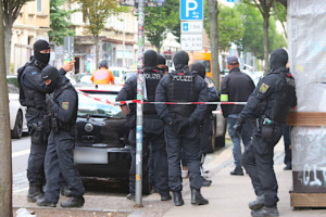 Großteils vermummte Polizisten stehen gruppiert hintere einer Absperrung.