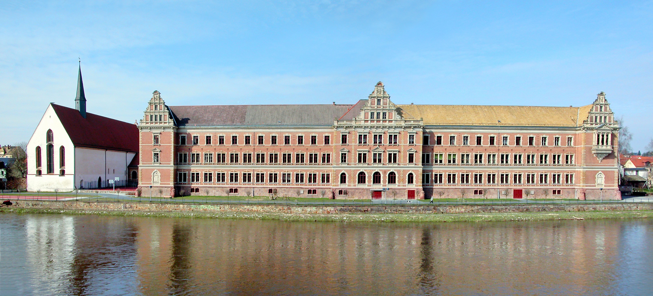 Gymnasium St. Augustin von der Mulde aus, links die Klosterkirche Grimma (Jörg Blobelt, CC BY-SA 4.0, https://commons.wikimedia.org/w/index.php?curid=77546024) 