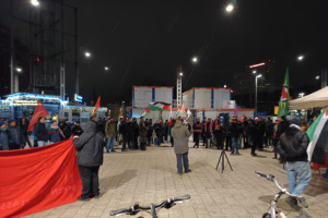 Demonstration mit Banner und Redner, Menschen haben sich davor versammelt.