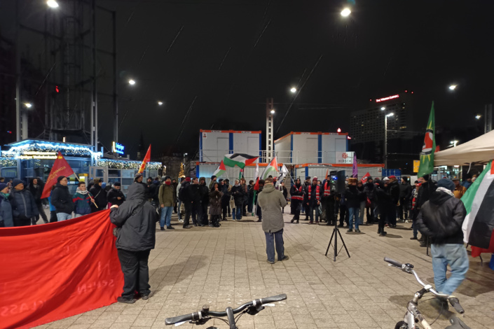 Demonstration mit Banner und Redner, Menschen haben sich davor versammelt.