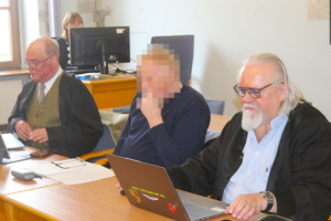 Angeklagter sitzt zwischen Verteidigern am Gericht.