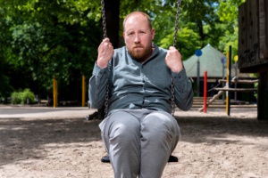 Mann sitzt auf Schaukel.