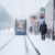 Schneefell an Haltestelle, Tram von hinten bei der Abfahrt, PKW auf separater Straße.