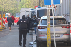 Polizeibeamte bei Razzia vermummt neben Wagen.