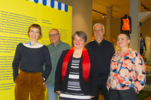 Personengruppe steht nebeneinander in einer Ausstellung.