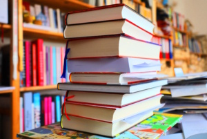 Gestapelte Bücher, im Hintergrund volle Regale.